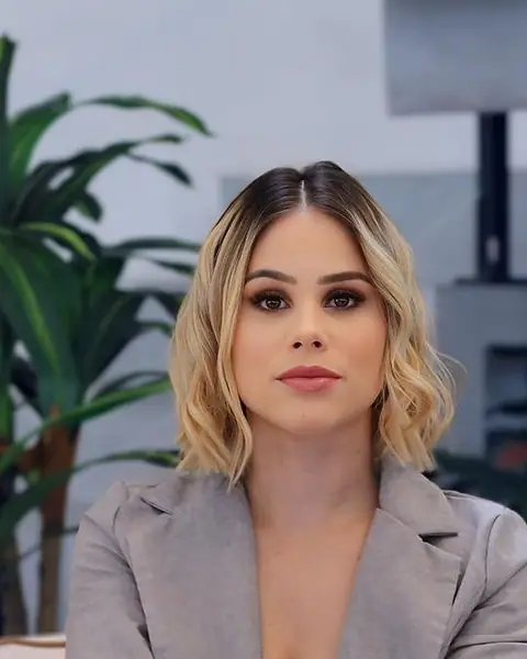 Dra. Letícia Moreira Amora, de terninho cinza, com os braços apoiados no joelho